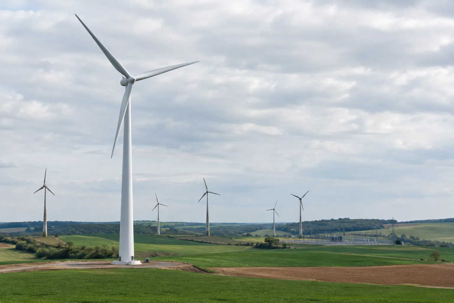 Une éolienne récente domine un parc où subsistent des turbines plus anciennes, avec un poste électrique au loin.